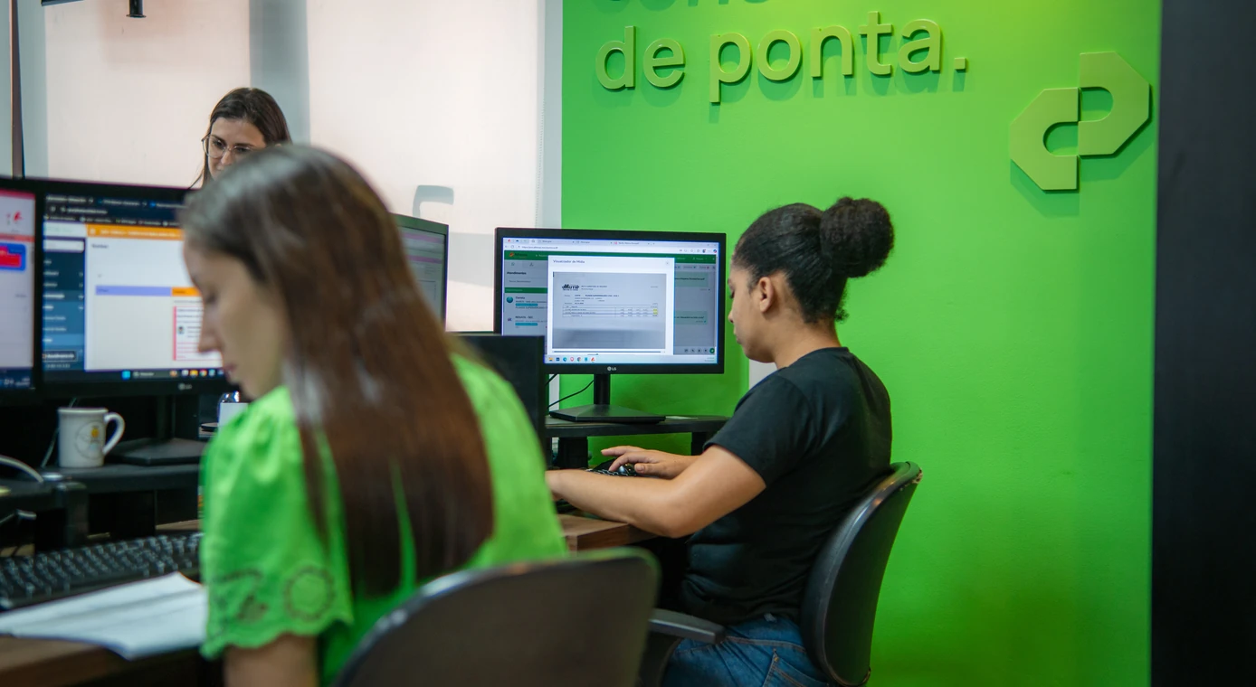 Profissionais da PCE trabalhando lado a lado diante da parede verde da empresa