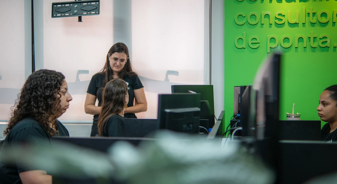 Profissional da PCE alinha o trabalho com colegas diante da parede verde da empresa
